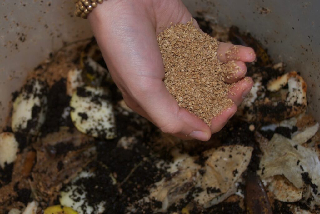Earth Bokashi being sprinkled over food waste inside a Bokashi bin